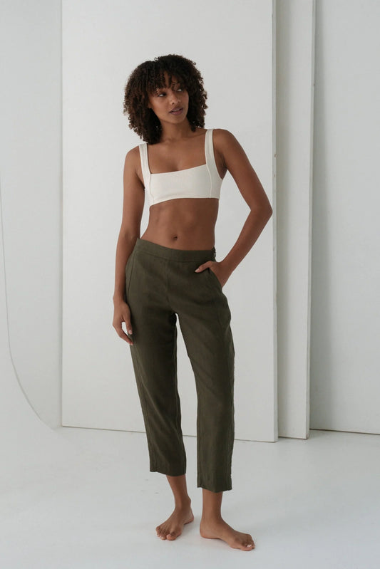 Woman wearing a white top and green linen trousers against a white background