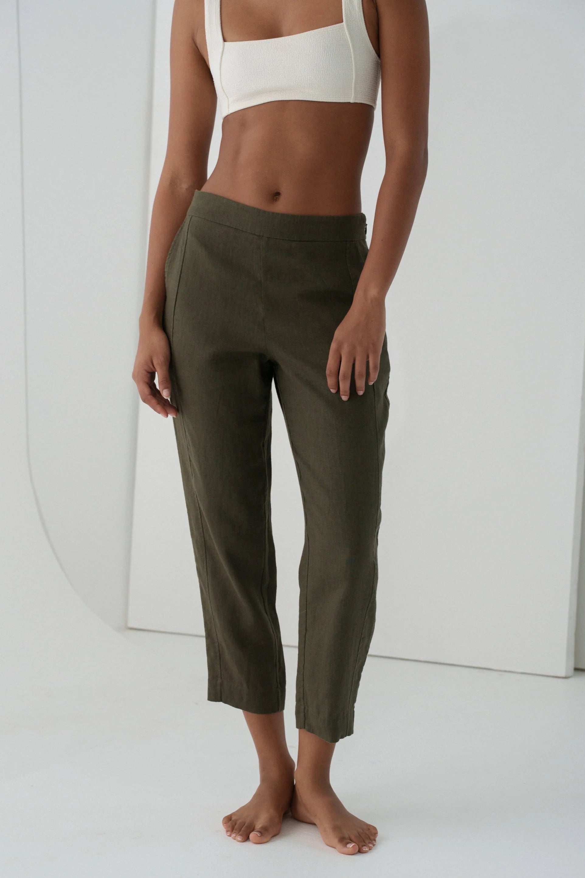 Person wearing olive green linen trousers and a white top on a white background