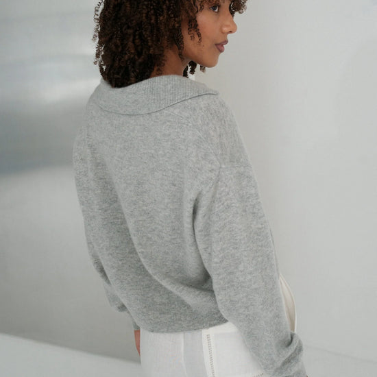Person wearing a gray sweater and white pants in a minimalistic setting