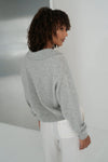 Person wearing a gray sweater and white pants in a minimalistic setting