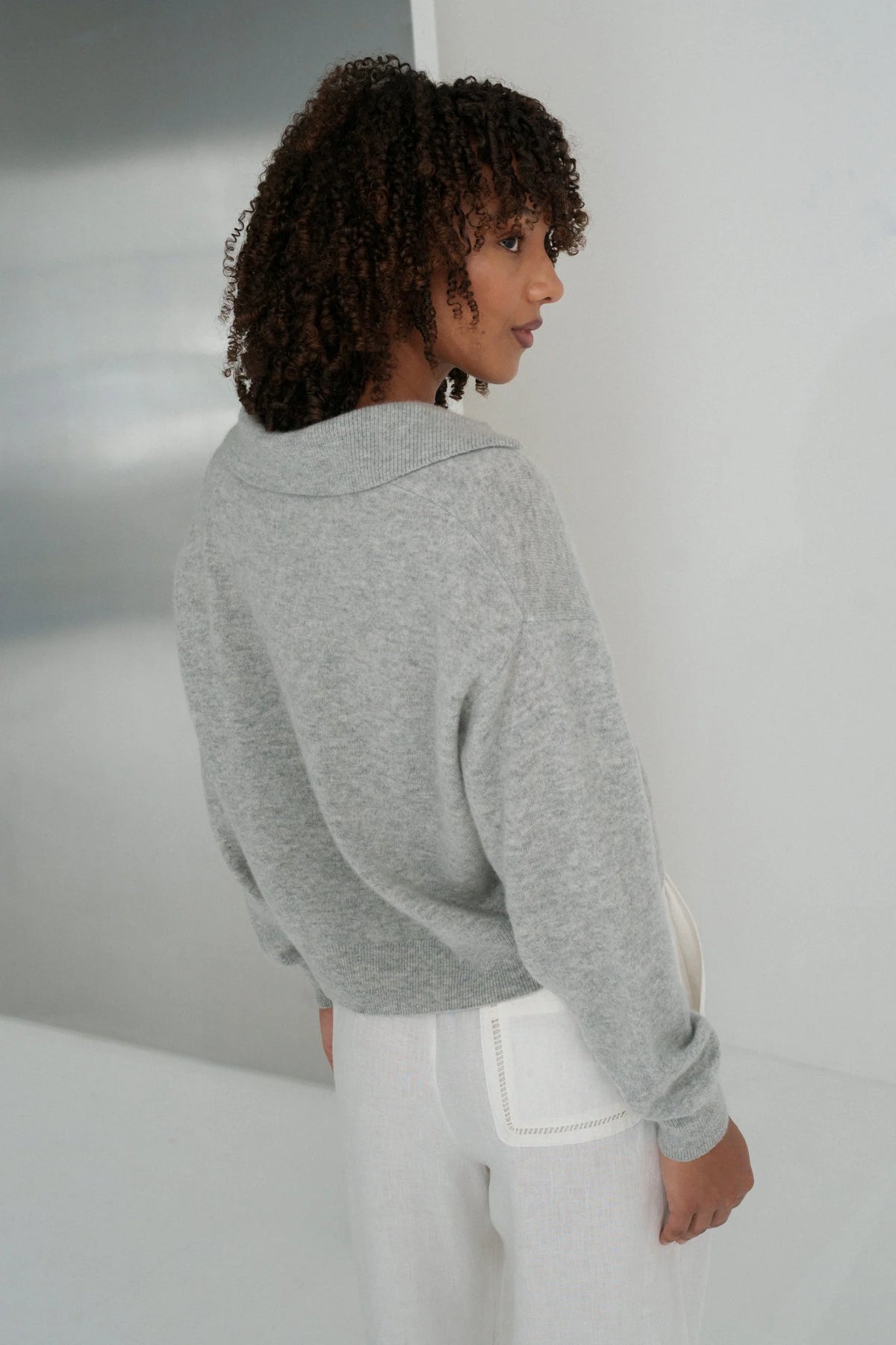 Person wearing a gray sweater and white pants in a minimalistic setting
