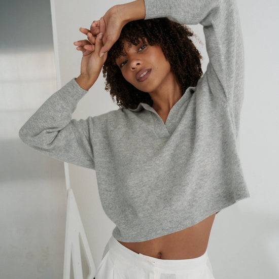 Woman wearing a gray sweater and white pants against a plain background