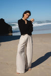 Woman in black sweater and light pants standing on a beach with ocean waves in the background