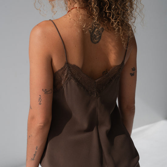 A woman shown from the back wearing a brown satin camisole with lace trim at the neckline, photographed in a studio setting.