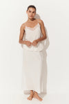A woman modeling a two-piece white lingerie set consisting of a camisole top with lace trim and a matching long skirt, set against a plain white studio background.