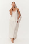 A woman modeling a two-piece white loungewear set consisting of a camisole top with lace trim and a matching long skirt, set against a plain white studio background.
