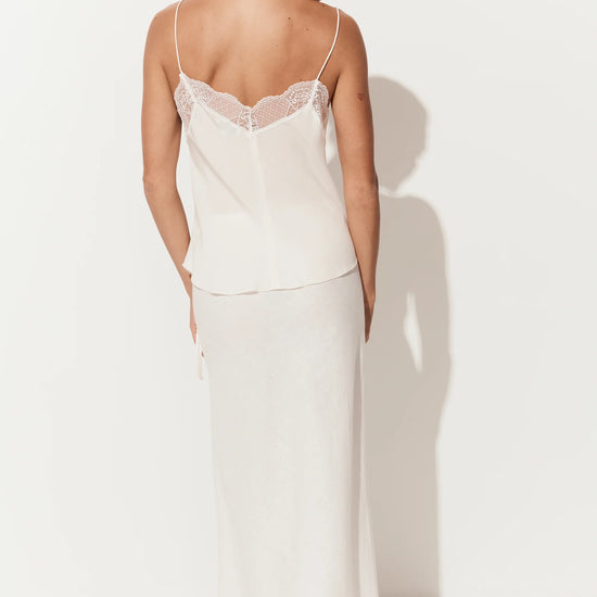 A woman shown from the back wearing a two-piece slip set consisting of a cream camisole with lace trim and a matching long skirt, set against a plain white studio background with a soft shadow.