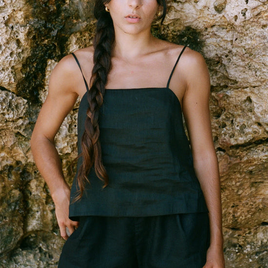 Woman wearing a black linen tank top and shorts against a stone wall.
