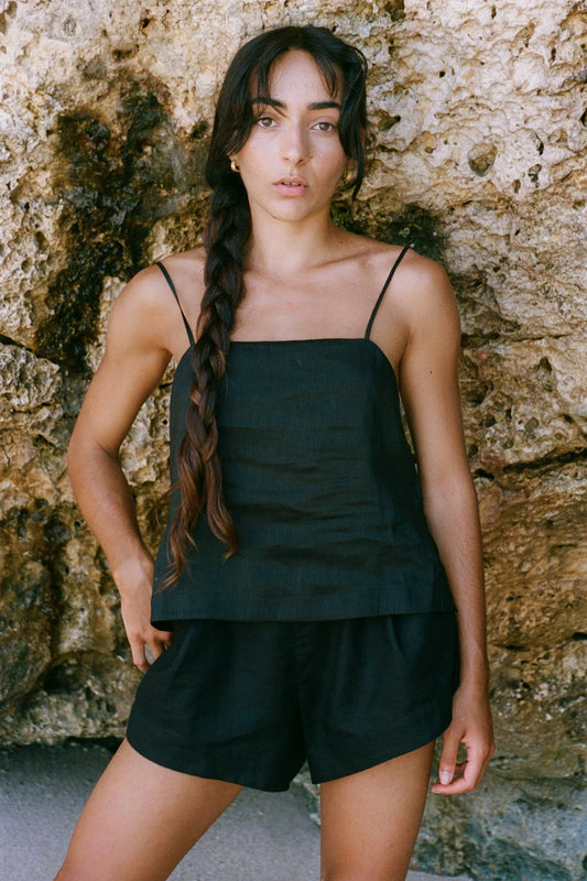 Woman wearing a black linen tank top and shorts against a stone wall.