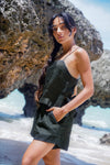 Woman in a black top and shorts standing on a rocky beach with ocean in the background