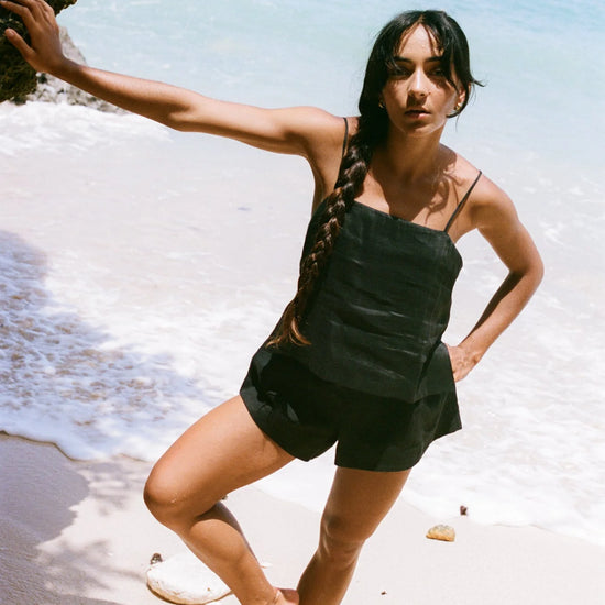 Woman standing on a beach holding a rock with clear blue water and sky in the background