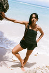 Woman standing on a beach holding a rock with clear blue water and sky in the background