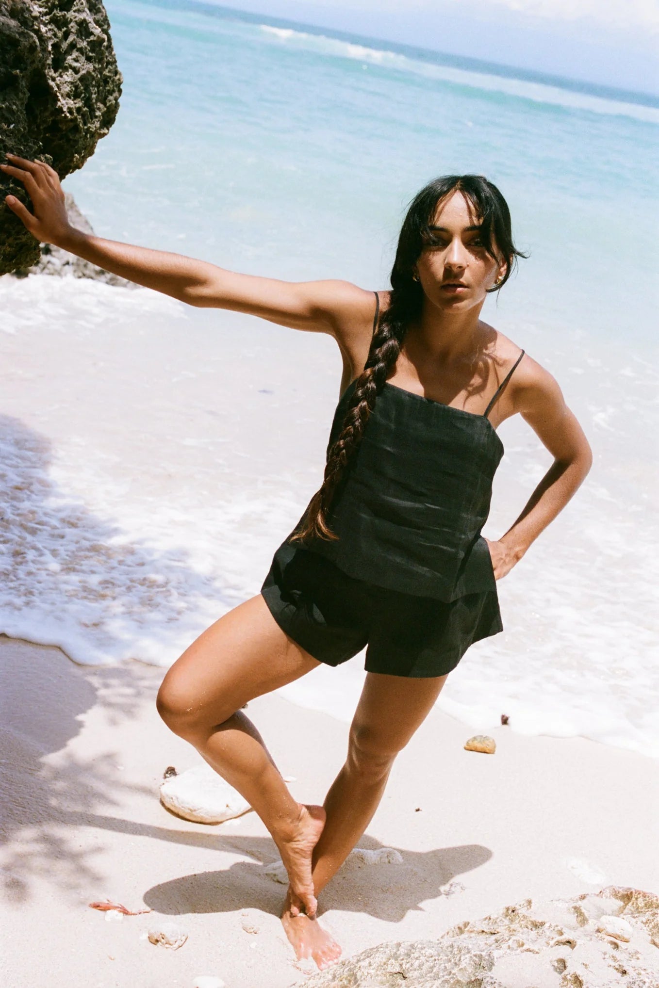 Woman standing on a beach holding a rock with clear blue water and sky in the background
