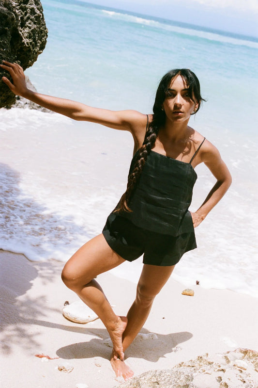 Woman standing on a beach holding a rock with clear blue water and sky in the background