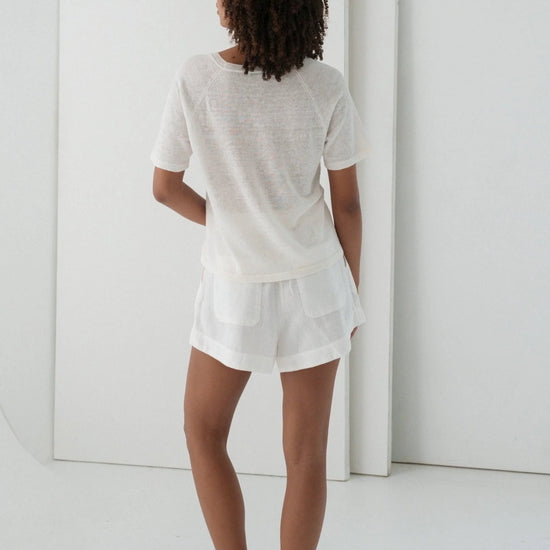Person wearing a white outfit standing in a minimalistic room.