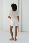 Person wearing a white outfit standing in a minimalistic room.