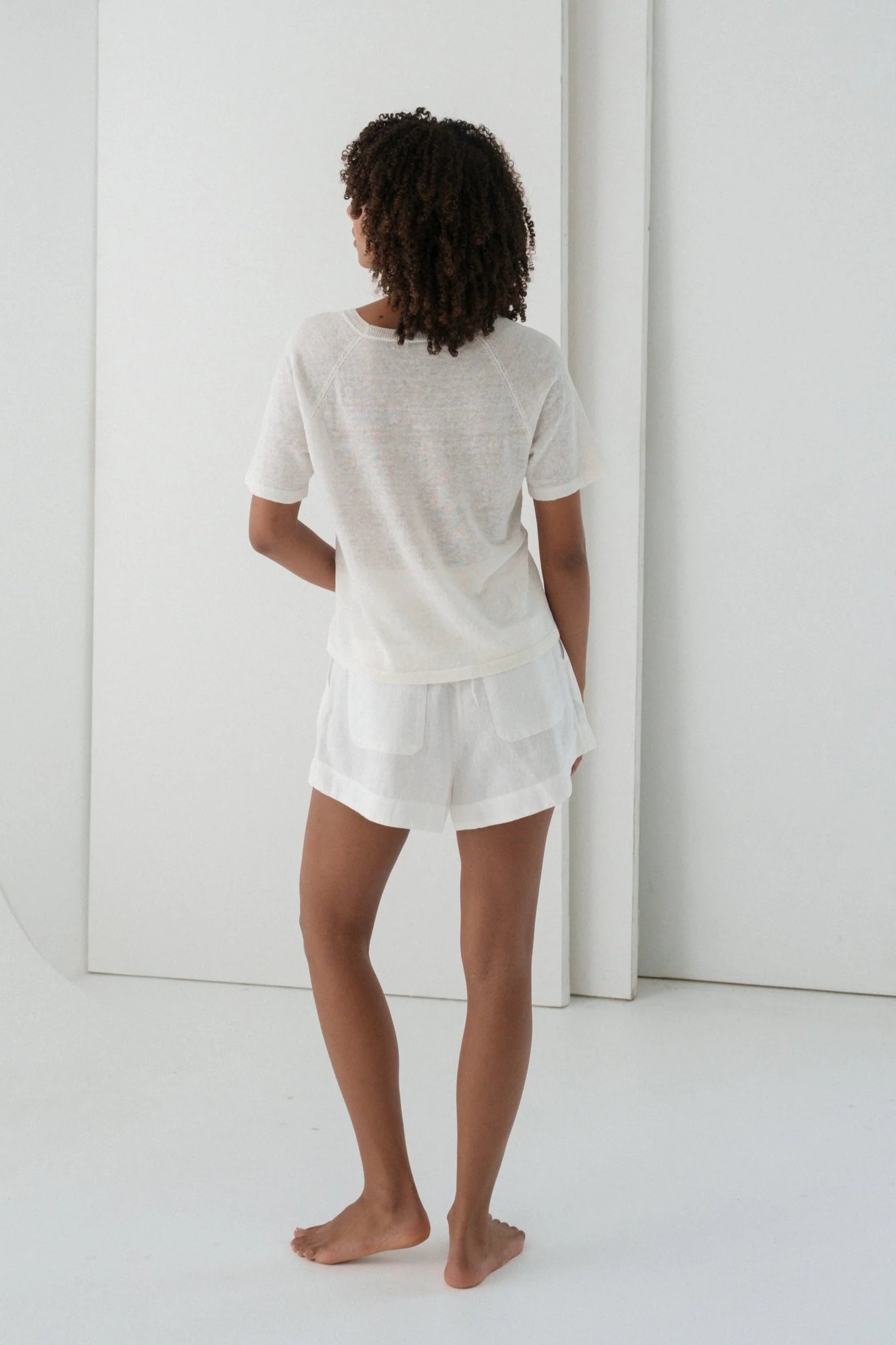 Person wearing a white outfit standing in a minimalistic room.