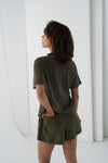 Person wearing an olive green outfit standing against a white background