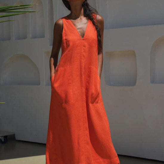Woman wearing an orange linen dress standing against a white wall with architectural elements.