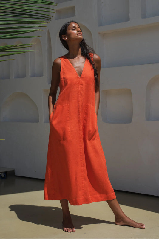 Woman wearing an orange linen dress standing against a white wall with architectural elements.