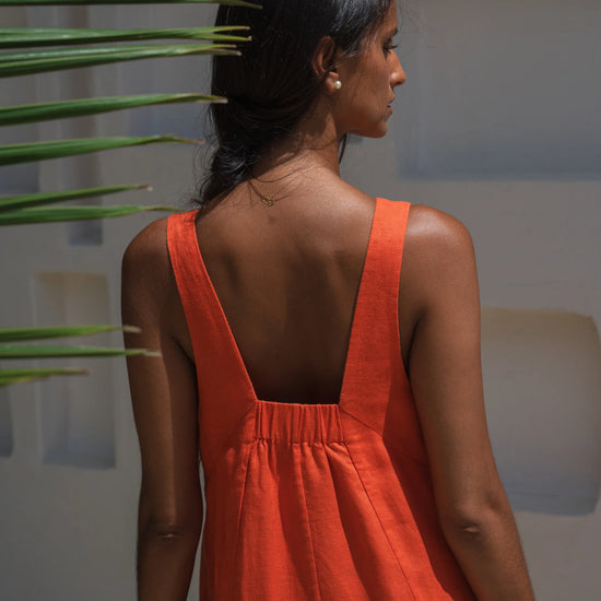 Woman wearing an orange linen dress with a plant in the background