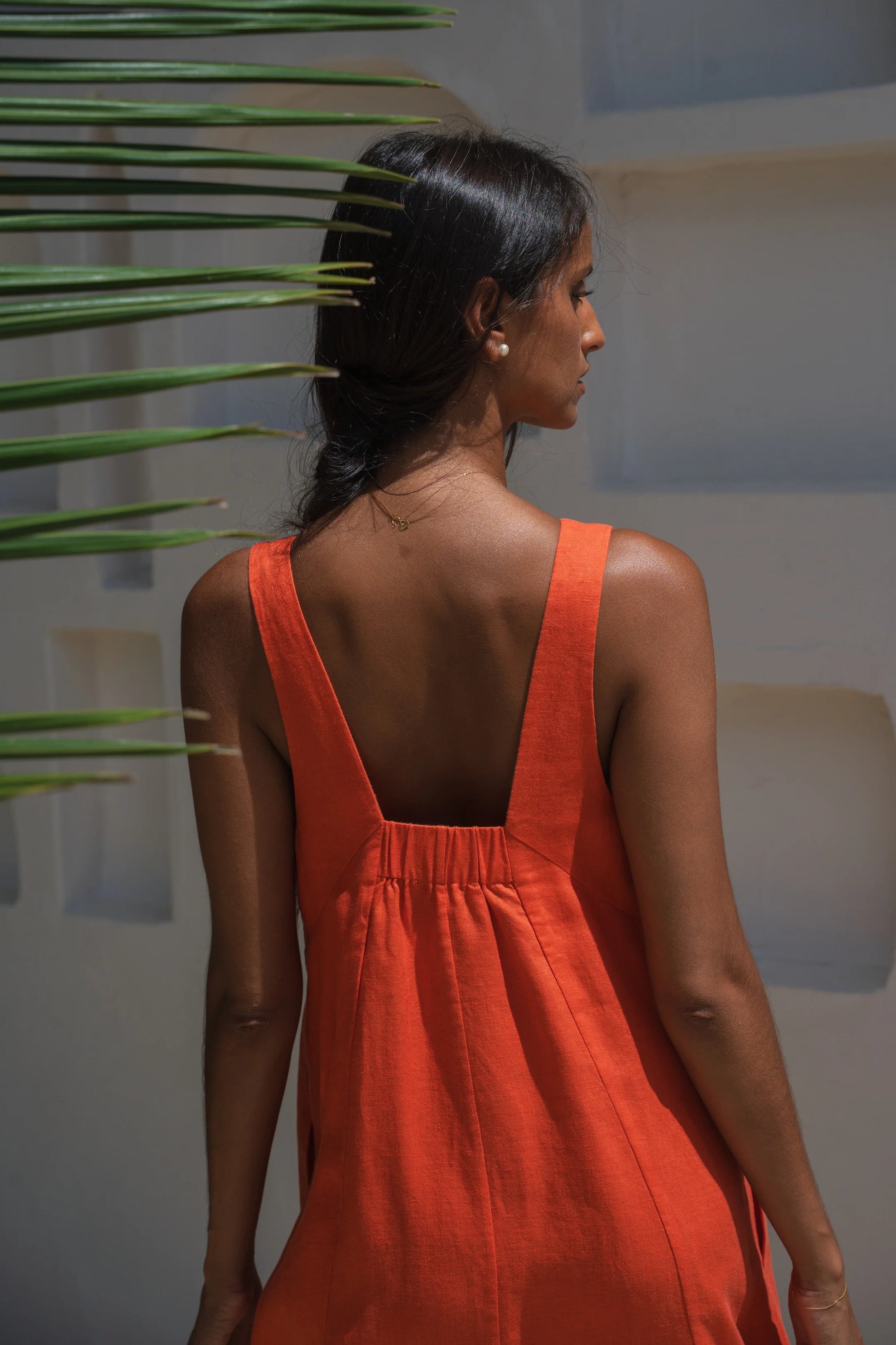 Woman wearing an orange linen dress with a plant in the background