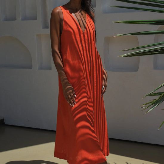 Woman in an orange linen dress standing against a white wall with architectural elements and greenery.