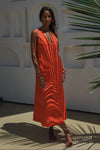Woman in an orange linen dress standing against a white wall with architectural elements and greenery.