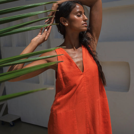 Woman in an orange linen dress holding a plant in a modern indoor setting