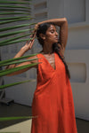 Woman in an orange linen dress holding a plant in a modern indoor setting