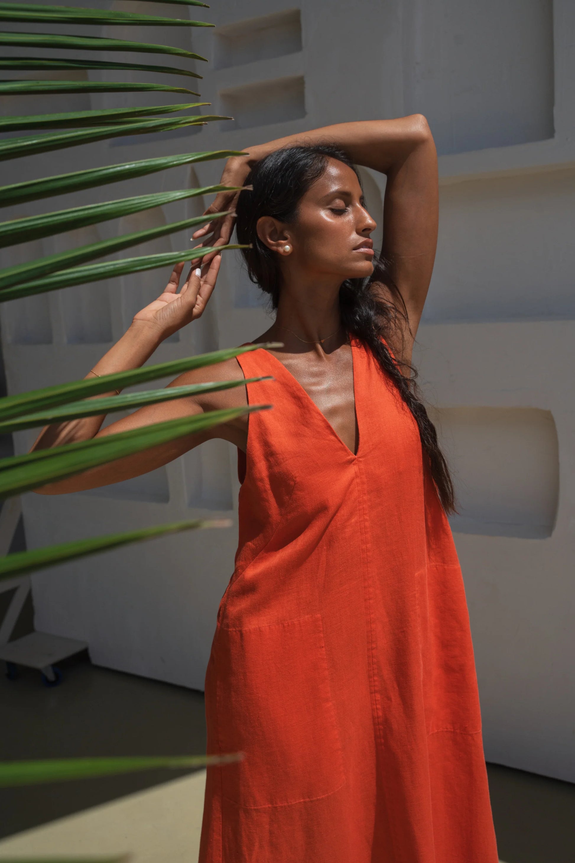 Woman in an orange linen dress holding a plant in a modern indoor setting