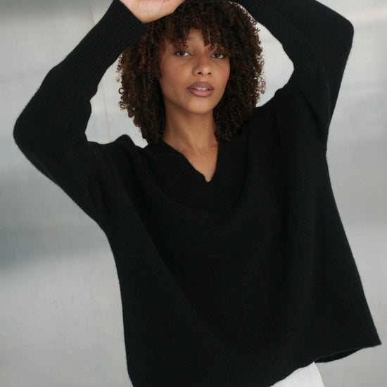 Woman wearing a black sweater with a white cloud design on a neutral background