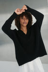 Woman wearing a black sweater with a white cloud design on a neutral background