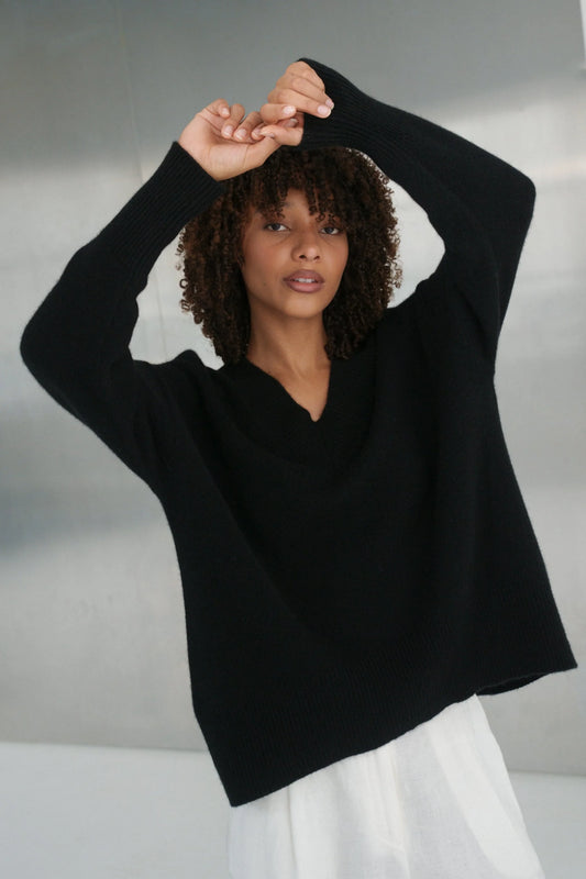 Woman wearing a black sweater with a white cloud design on a neutral background