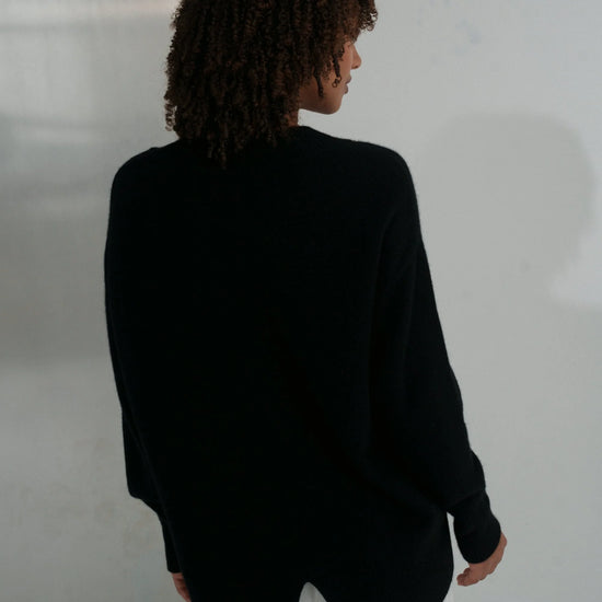 Person wearing a black blazer and white pants against a plain background