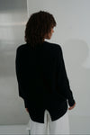 Person wearing a black blazer and white pants against a plain background