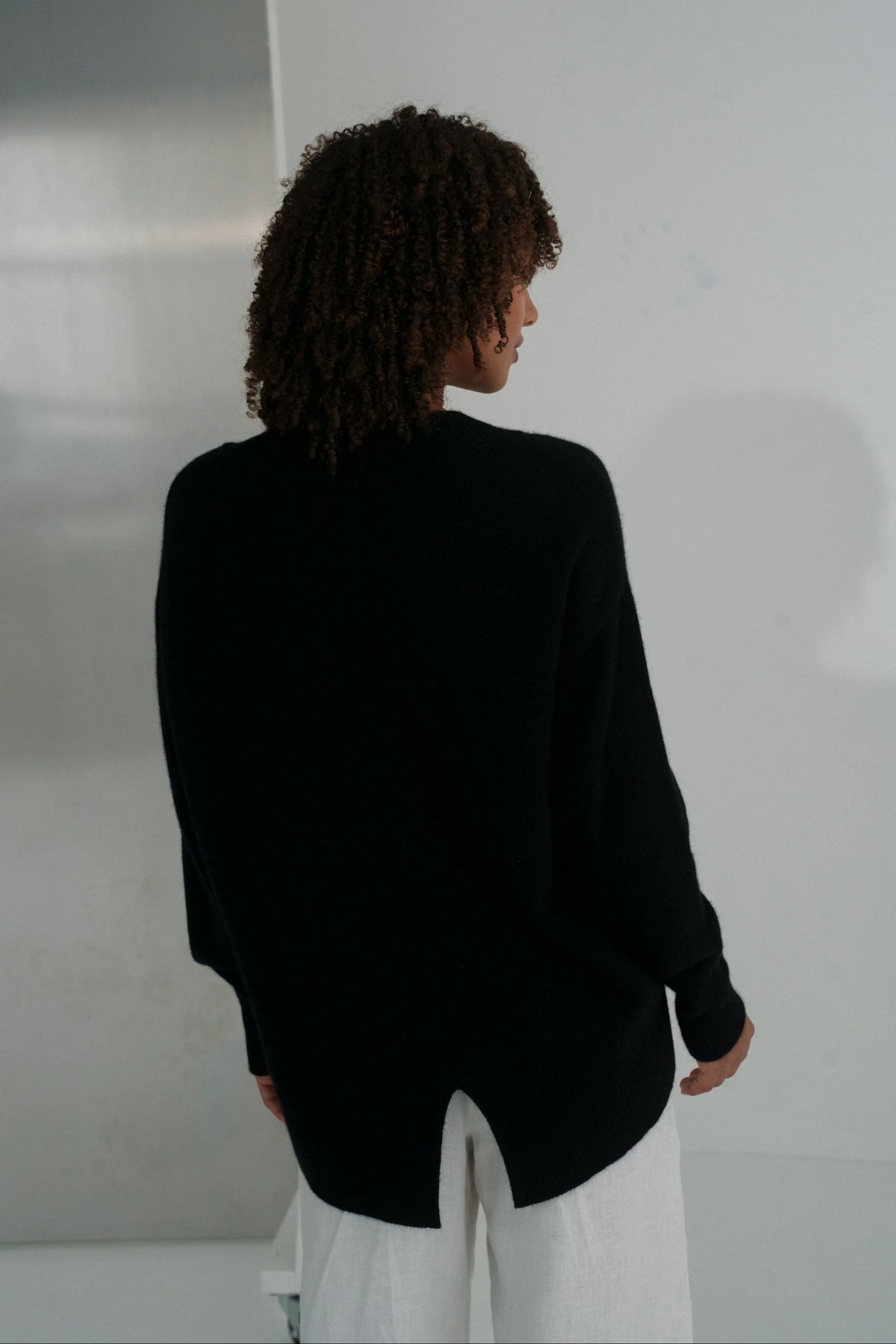 Person wearing a black blazer and white pants against a plain background