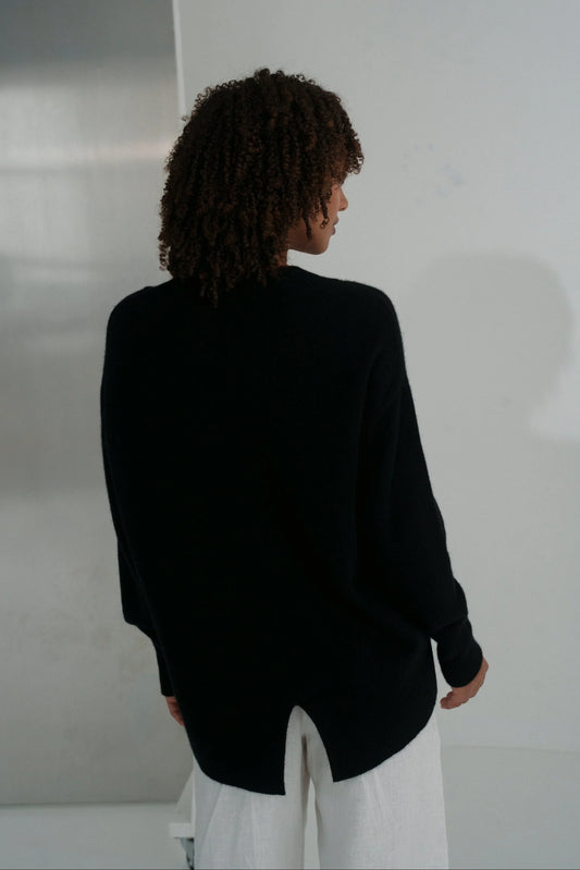 Person wearing a black blazer and white pants against a plain background