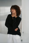 Woman wearing a black sweater and white pants against a neutral background