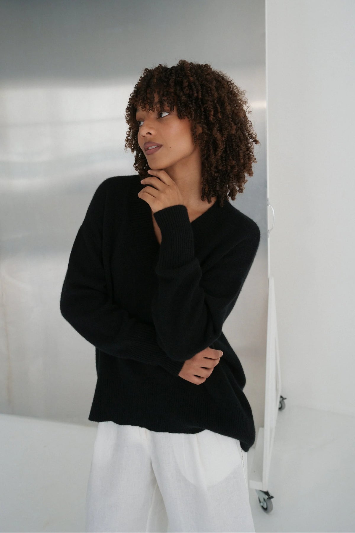 Woman wearing a black sweater and white pants against a neutral background