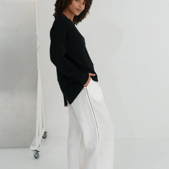 Person wearing a black sweater and white pants against a white background