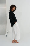 Person wearing a black sweater and white pants against a white background
