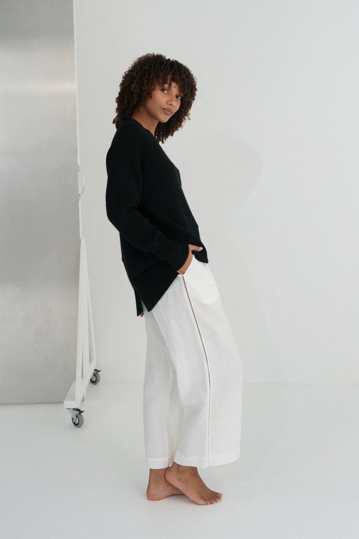 Person wearing a black sweater and white pants against a white background