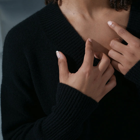Person wearing a black sweater with hands adjusting the neckline against a blurred background