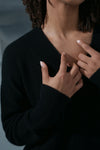 Person wearing a black sweater with hands adjusting the neckline against a blurred background