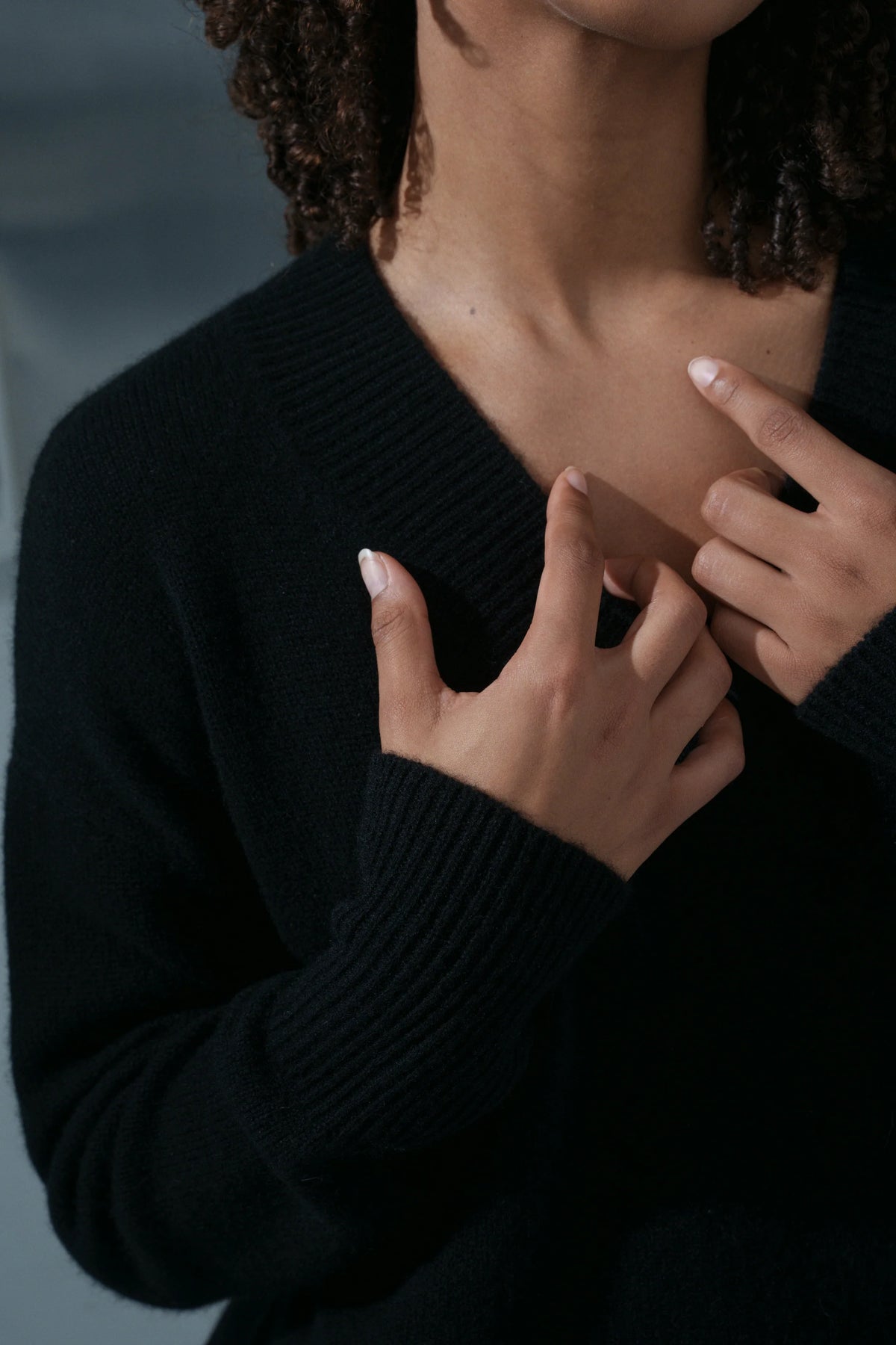 Person wearing a black sweater with hands adjusting the neckline against a blurred background