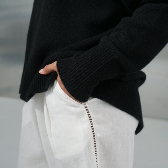 Person wearing a black sweater and white pants with a blurred background