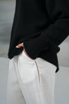 Person wearing a black sweater and white pants with a blurred background