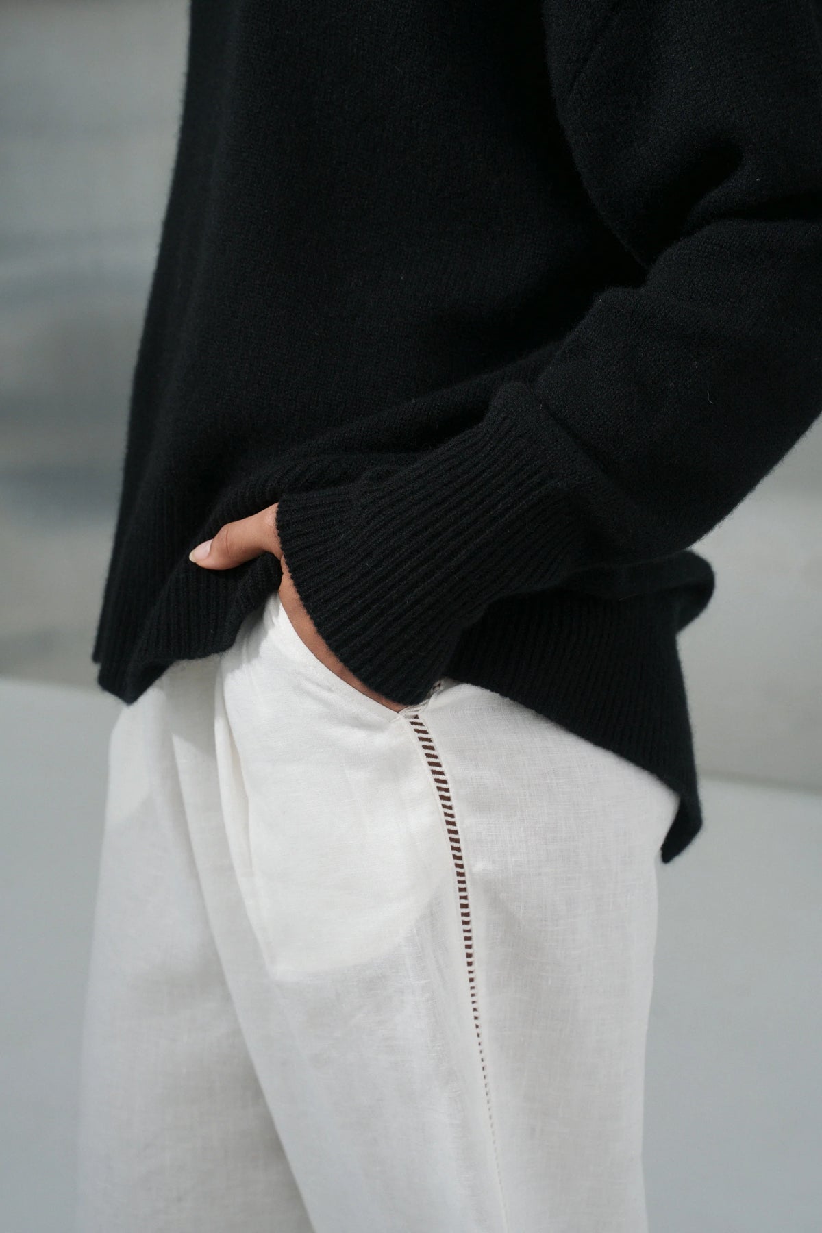 Person wearing a black sweater and white pants with a blurred background