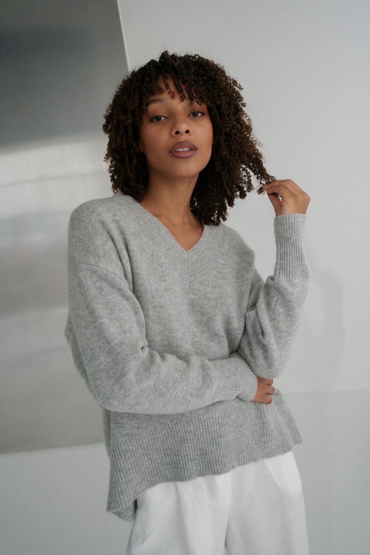 Woman wearing a gray sweater and white pants against a neutral background
